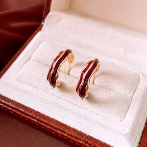 Deep red enamel wavy C-shape earrings with gold plating on a warm display surface