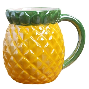 Vibrant yellow pineapple shaped ceramic coffee mug with green leaf handle on white background