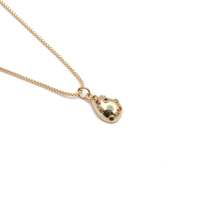 Collana con pendente a goccia dorata con zirconi colorati su sfondo bianco