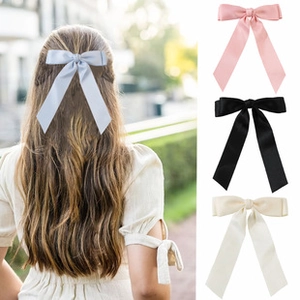 Detail showing oversized satin ribbon bow hair clips in pink, black, beige, and blue colors