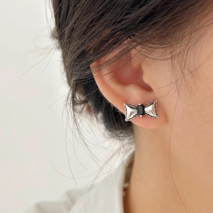 Macro view of a silver bow earring with a black rectangular zircon stone and spotted details
