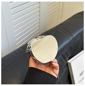 Detail of a mini heart-shaped silver mirror bag with fine chain strap held in hand