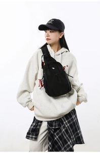 Detail of black nylon sling bag featuring drawstring closure and metal kitten logo