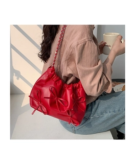Red ruched PU leather bag with bow details and silver chain strap on model's shoulder