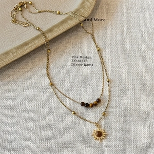 Double-layered tiger eye sunflower necklace in gold finish on neutral textured background