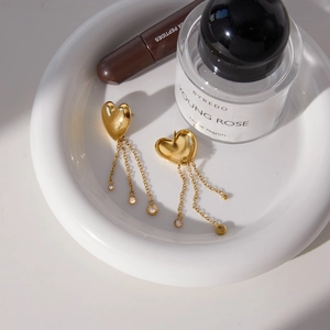 Detail of gold heart earrings with chain tassels and crystal charms on a ceramic tray