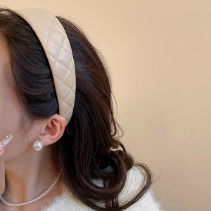 Close-up of a beige quilted leather headband worn on wavy hair with pearl accessories