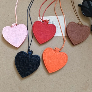Flat lay of heart-shaped lychee leather pendants in five colors on a kraft paper backdrop