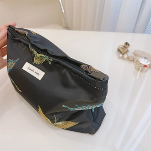 Detailed view of butterfly embroidery and zipper on a black jacquard cosmetic bag