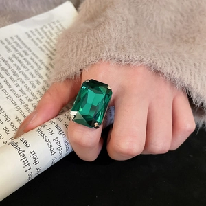Close-up of emerald-cut green crystal ring with silver claw setting on model finger