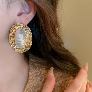 Macro view of vintage gold textured oval earrings with pearl inlay worn by a model