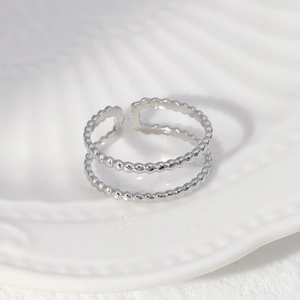 Detailed close-up of a silver double-layer beaded open ring on a white textured tray