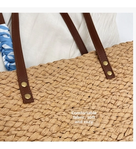 Detail of woven straw tote bag with brown leather handles and striped ribbon accent