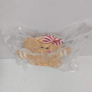 Gingerbread man plush pillow with red bowtie detail inside protective clear plastic wrap
