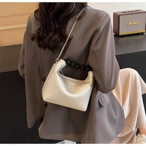 Silver mini dumpling bag featuring black pearl handle and metallic chain strap on model