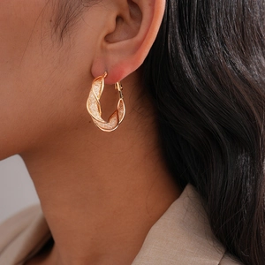 Detailed close-up of a gold twisted hoop earring with textured cross-grid finish on a model