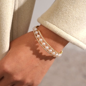Detailed macro view of a three-layer faux pearl and rhinestone gold cuff bracelet on wrist