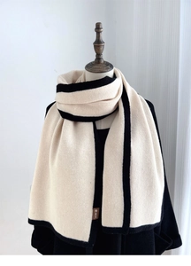 Detail of beige knit scarf with black stripes and brown leather brand label on the hem