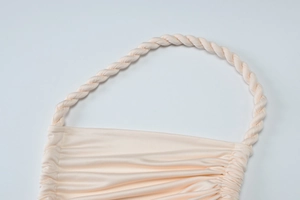 Close-up of light apricot pleated dress with woven rope straps and silky fabric texture