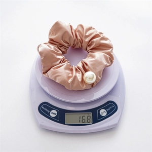 Detail shot of champagne satin scrunchie with white pearl pendant on a digital scale