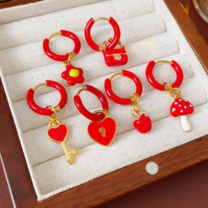 Detail view of gold hoop earrings with red enamel flower and heart charms in a jewelry box