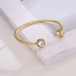 Macro detail of gold beaded open bangle with round clear crystals on magazine background