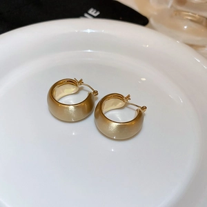 Detailed top view of gold hoop earrings with brushed metal finish on white ceramic plate