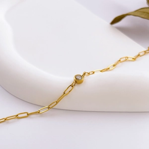 Detailed shot of golden paperclip chain bracelet with round clear gemstone on white base