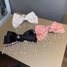 Detailed view of satin bow hair clips with rhinestones and fringe in white, black, and pink