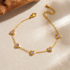 Détail d'un bracelet cœur plaqué or avec cristaux violets sur fond de sable texturé