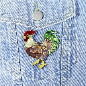Handmade acrylic rooster brooch with amber texture on a denim jacket pocket
