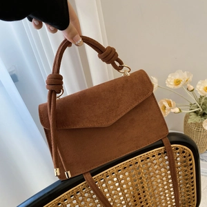 Brown faux suede crossbody bag with knotted handle and gold hardware on a rattan chair