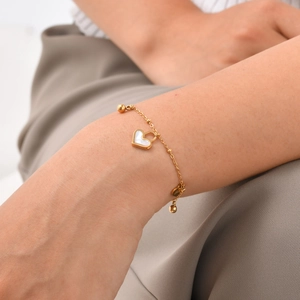 Detail of gold cross chain bracelet featuring shell heart charm and metallic beads