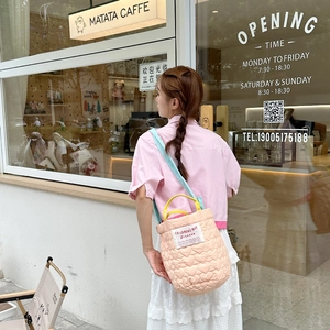 Quilted pink bucket bag with yellow handles and blue strap worn by model in cafe setting