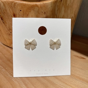 Detailed close-up of bow earrings with faux pearls and rhinestones on white display card