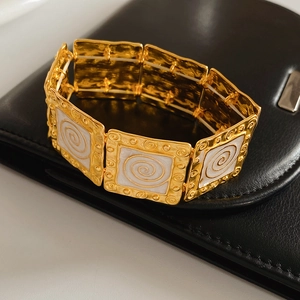 Detail of vintage gold square link bracelet with white spiral enamel on black leather