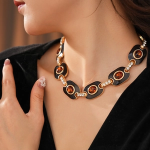 Close-up of vintage gold necklace with black enamel, amber stone, and sparkling rhinestones