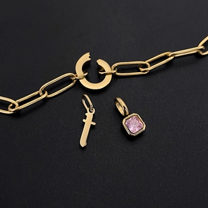 Nahaufnahme einer goldenen Büroklammerkette mit rosa Stein und Kleinbuchstaben-'t'-Anhänger.