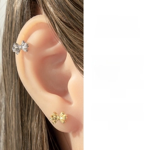 Detailed close-up of bow-shaped cartilage piercings in gold and silver micro-set with zircon