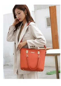 Detail of an orange leather tote bag with gold hardware held by a model in a beige suit
