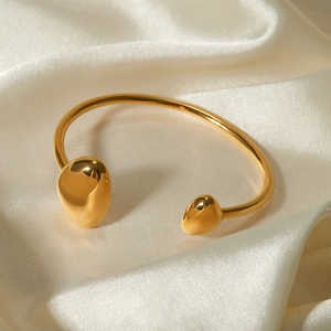 Dettaglio di un bracciale rigido in oro 18k su elegante tessuto di seta crema