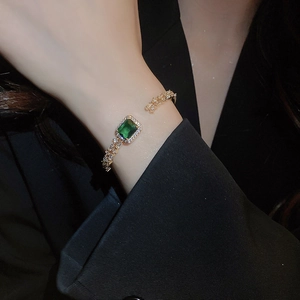 Close-up of elegant gold bangle featuring square emerald zircon and sparkling pave stones