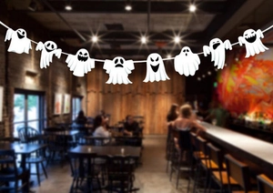 Close-up of white Halloween ghost paper banner with diverse expressions in a dimly lit bar