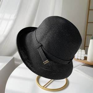 Elegante cappello di paglia nero con fibbia dorata su un supporto decorativo bianco