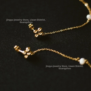 Detail of gold clover stud with trailing pearl chain on textured black fabric background
