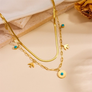 Detail of layered gold bird necklace with turquoise charms on silk and marble background