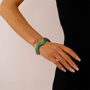 Detail of green wavy acrylic bangle with marble pattern texture on a female model