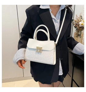 Detailed view of a white crocodile embossed handbag with gold buckle on a model in a blazer