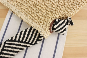 Detail of woven paper straw bag with checkered strap and reinforced leather metal eyelets