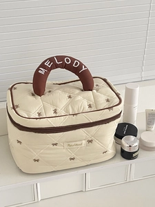Dettaglio della borsa da trucco trapuntata crema con fiocchi caffè e manico marrone
